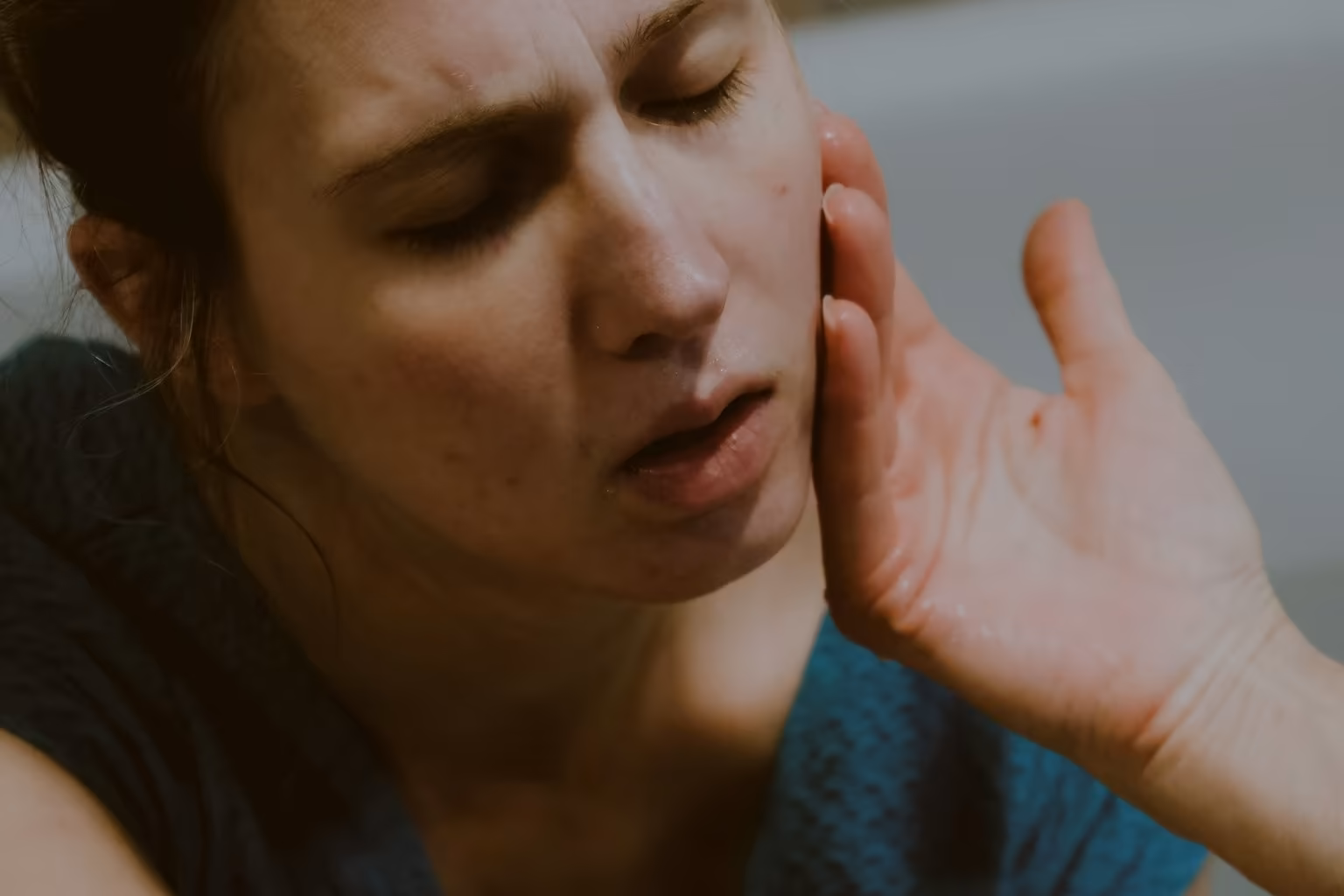 Woman resting a hand along her jaw and cheek during facial pain