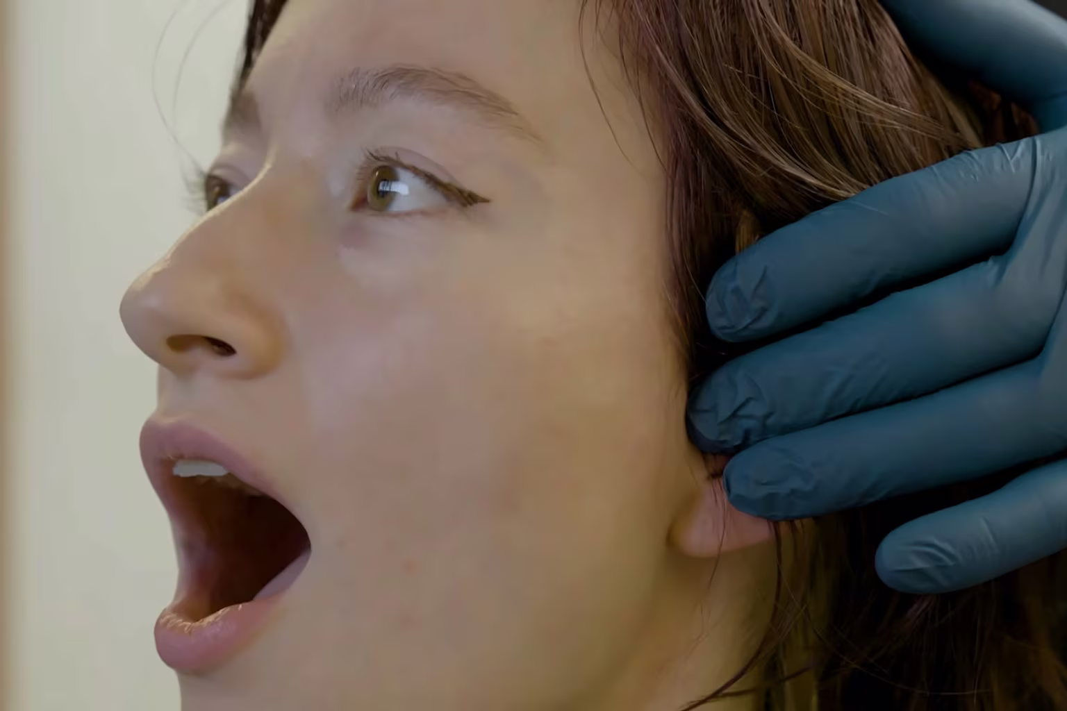 Gloved hand checking a patient's jaw joint as she opens wide during an evaluation